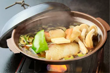 熱々の土鍋で煮込まれる魚と野菜の鍋。
