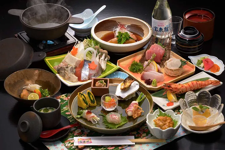 豪華な会席料理の膳。刺身、焼き魚、煮物、揚げ物などが彩りよく並んでいる。
