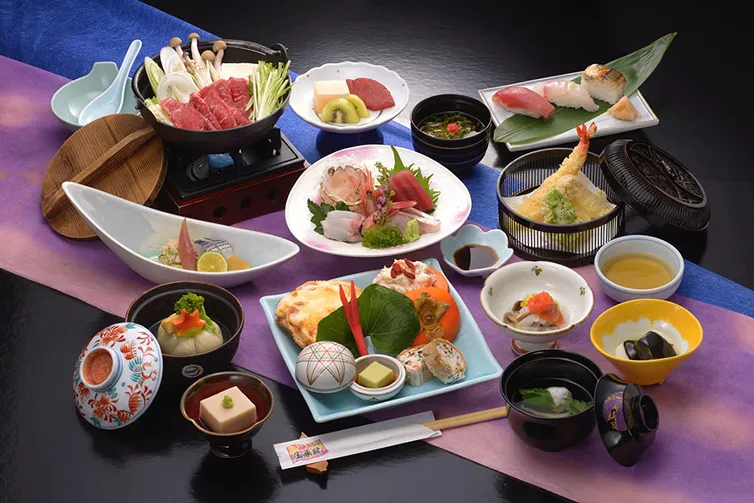 豪華な会席料理の膳。刺身、焼き魚、煮物、揚げ物、鍋物などが彩りよく並んでいる。