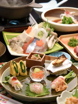 テーブルに並べられた様々な料理。鍋料理、刺身、焼き魚、煮物など、彩り豊かで豪華な食事が楽しめる。