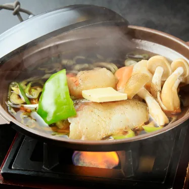 土鍋で煮込まれた料理。魚の切り身や野菜がだし汁の中で煮えている。