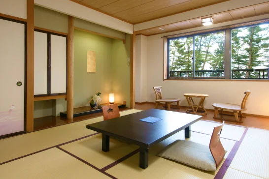 和室の室内。畳敷きの部屋に、黒いテーブルと座椅子が置かれている。奥には障子があり、外の緑が見える。